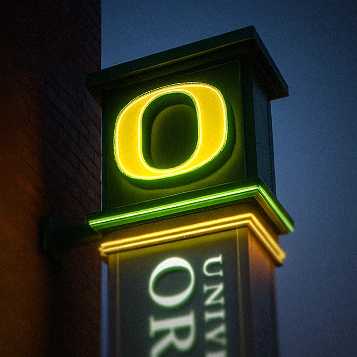 Illuminated University of Oregon blade sign glowing at dusk